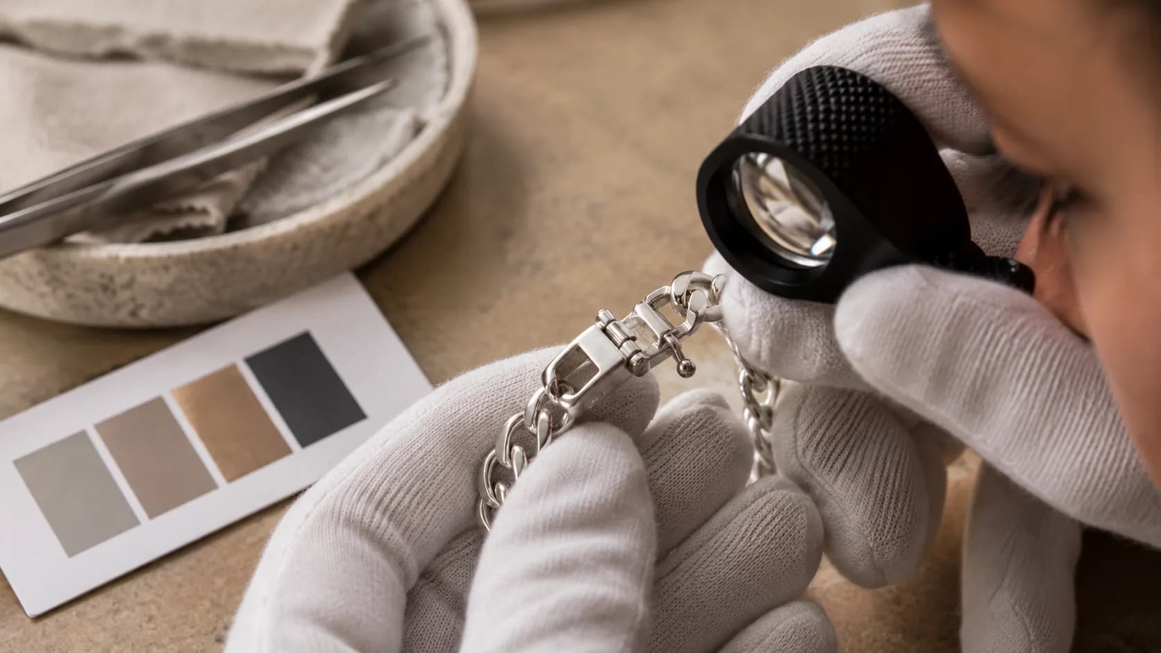 Gloved reviewer inspecting an unbranded silver bracelet clasp with a jeweler loupe